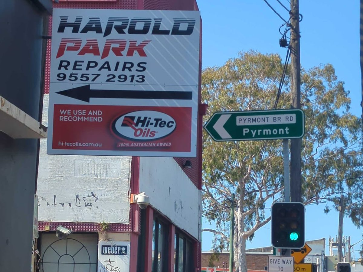 The corner of the Harold Park Repairs building, with the pylon sign beside the green Pyrmont Bridge Road street sign and the traffic lights at the intersection